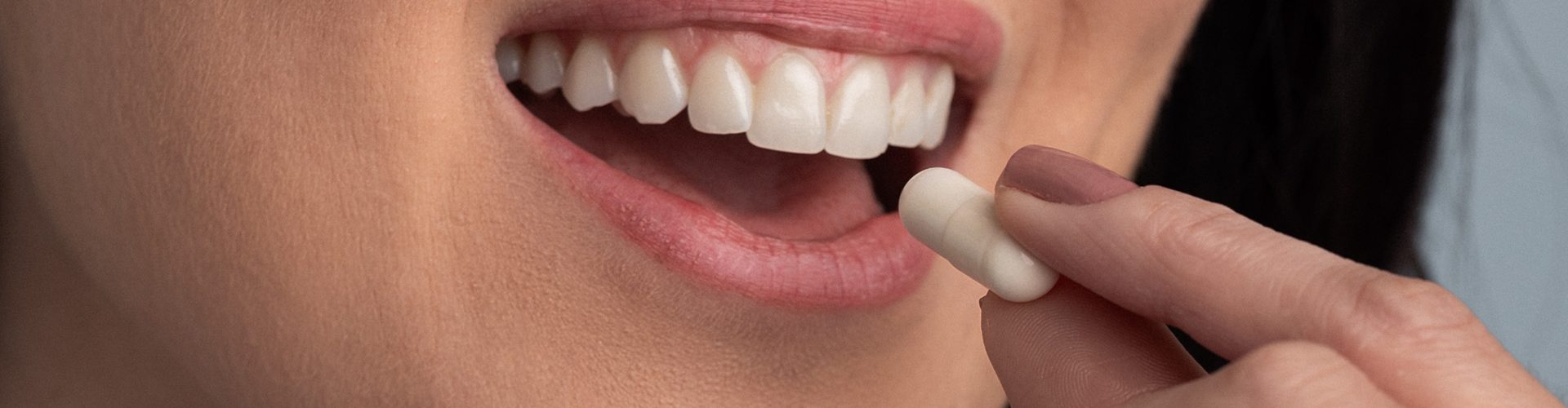 Mulher sorrindo enquanto leva um comprimido branco à boca, ilustrando o momento de tomar um probiótico