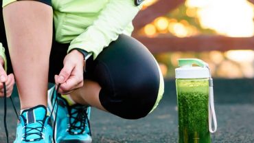 Atleta amarrando o tênis com um shake de receitas pré-treino ao lado