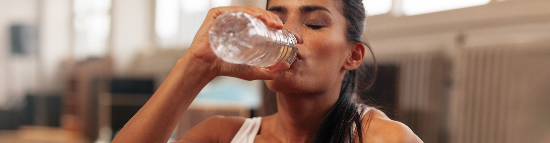 Mulher de tope branco sentada no chão bebendo água para a hidratação do cérebro.